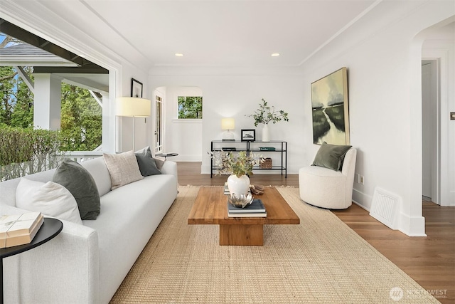 living area with wood finished floors, visible vents, recessed lighting, arched walkways, and ornamental molding