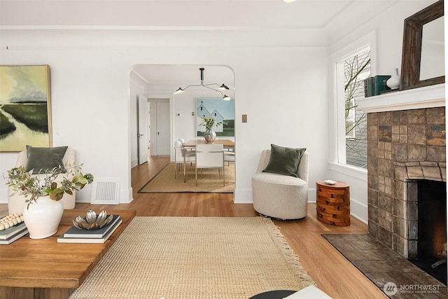 living room featuring visible vents, a fireplace with flush hearth, baseboards, and wood finished floors