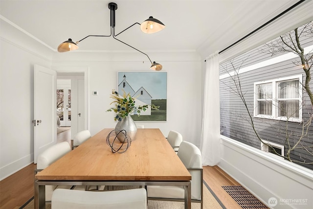 dining space with light wood-type flooring, visible vents, baseboards, and ornamental molding