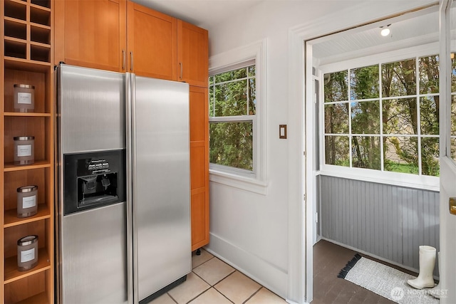 kitchen featuring light tile patterned flooring, baseboards, stainless steel refrigerator with ice dispenser, and brown cabinets