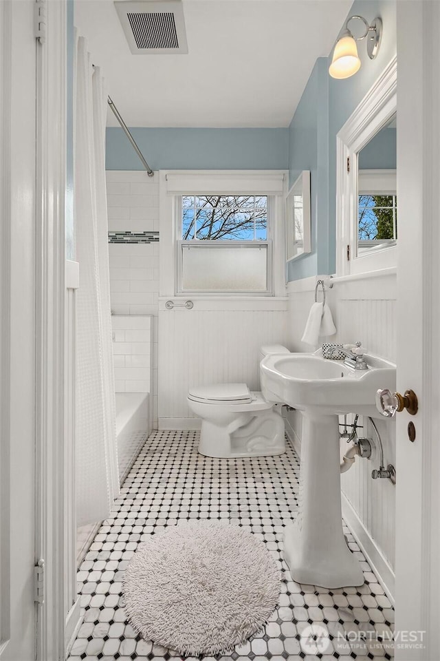 full bath featuring visible vents, toilet, a wainscoted wall, and shower / tub combo with curtain