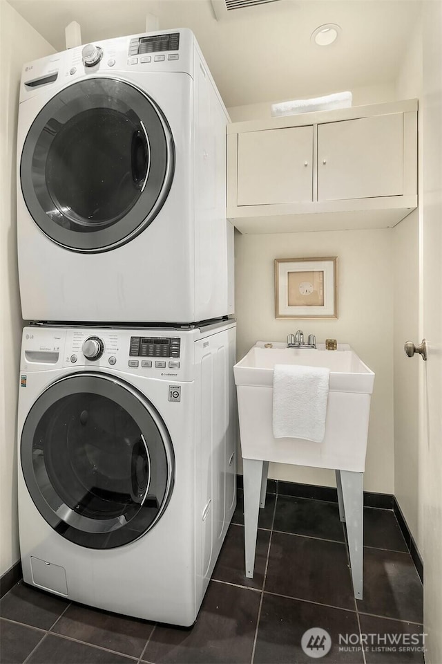 washroom featuring dark tile patterned flooring, cabinet space, stacked washer and clothes dryer, and baseboards