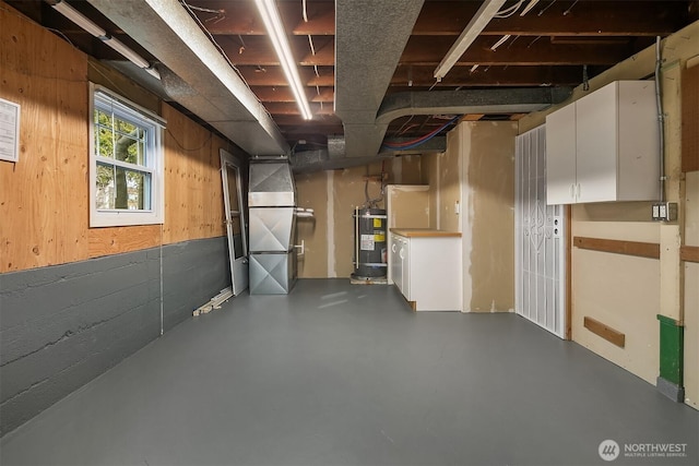 basement with heating unit, electric water heater, and wooden walls