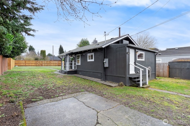 rear view of house with entry steps, a yard, and a fenced backyard