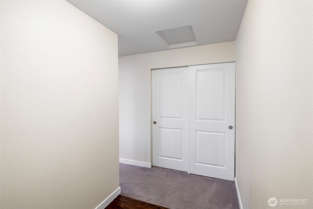 corridor with attic access, baseboards, and dark colored carpet