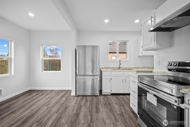 kitchen with a healthy amount of sunlight, dark wood finished floors, a sink, appliances with stainless steel finishes, and wall chimney exhaust hood