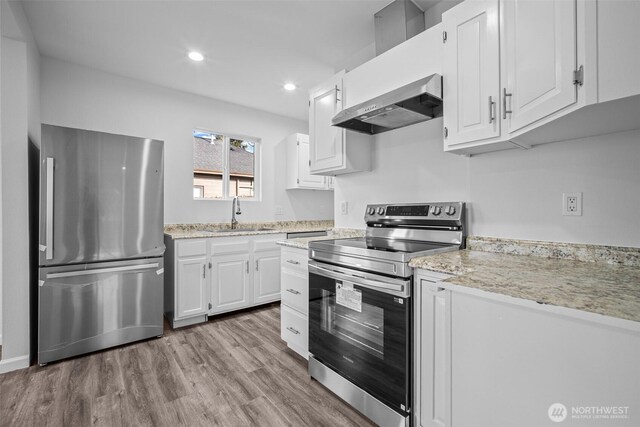 kitchen with wood finished floors, a sink, appliances with stainless steel finishes, white cabinetry, and wall chimney range hood