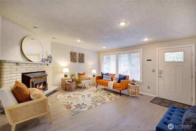 living area with a brick fireplace, baseboards, recessed lighting, wood finished floors, and a textured ceiling