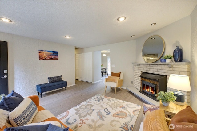 living area with a textured ceiling, wood finished floors, a fireplace, baseboards, and a textured wall