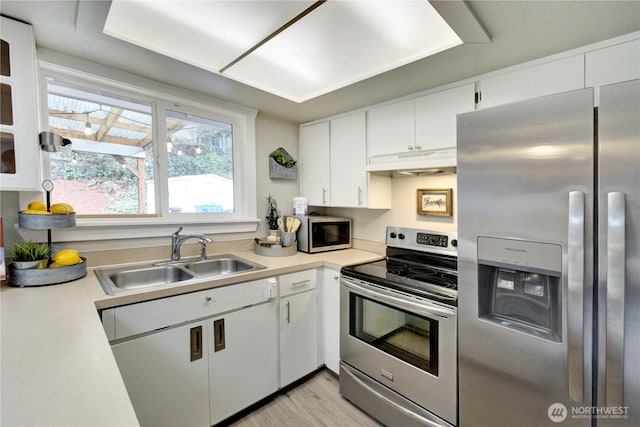 kitchen with a sink, stainless steel appliances, light countertops, under cabinet range hood, and white cabinetry