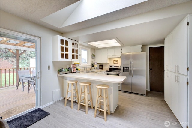 kitchen with lofted ceiling, a peninsula, a sink, appliances with stainless steel finishes, and light wood-type flooring