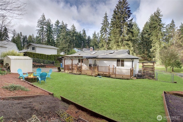 rear view of house with a deck, fence, a yard, a fire pit, and an outdoor structure