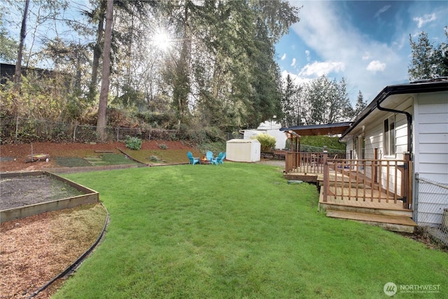 view of yard featuring a deck, a fenced backyard, an outbuilding, a storage unit, and a garden