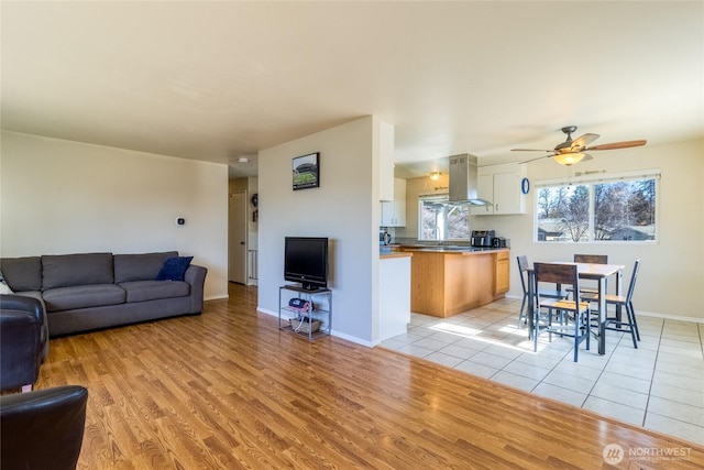 living area featuring light wood-type flooring, baseboards, and ceiling fan