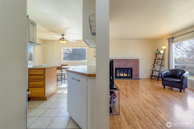 kitchen featuring light wood finished floors, open floor plan, a brick fireplace, and a ceiling fan