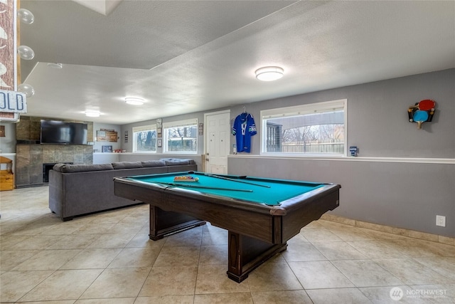 game room with a textured ceiling, light tile patterned flooring, and a tiled fireplace