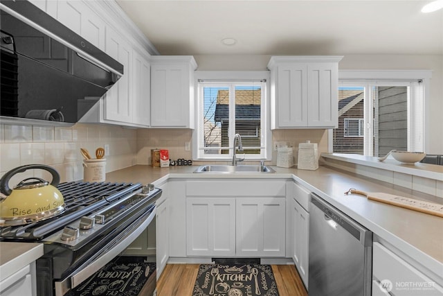 kitchen featuring black range with gas stovetop, light countertops, stainless steel dishwasher, white cabinetry, and a sink