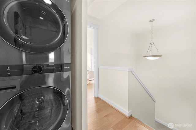 clothes washing area with laundry area, stacked washing maching and dryer, baseboards, and wood finished floors