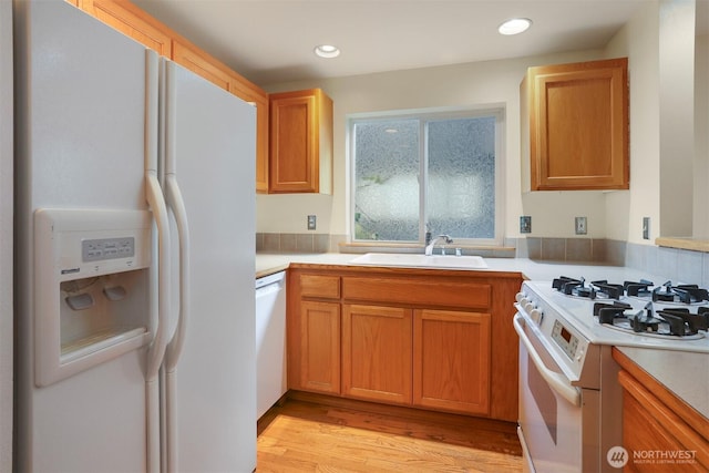 kitchen with light countertops, recessed lighting, light wood-style flooring, white appliances, and a sink