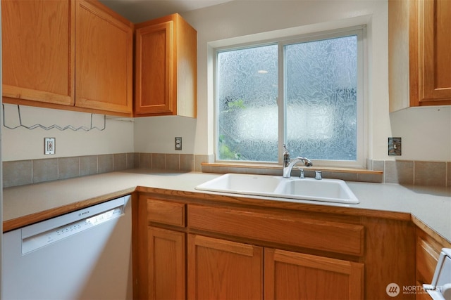 kitchen with dishwashing machine, brown cabinetry, light countertops, and a sink