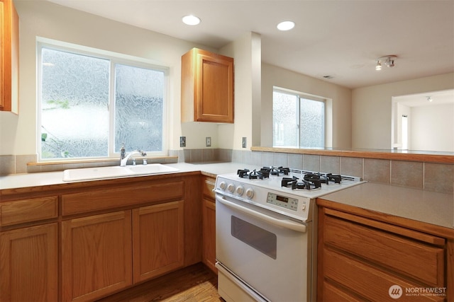 kitchen with white gas stove, recessed lighting, a sink, light countertops, and brown cabinets