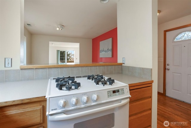 kitchen with visible vents, backsplash, wood finished floors, light countertops, and white gas range