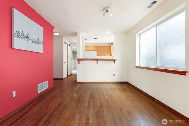 unfurnished living room with visible vents, baseboards, and wood finished floors