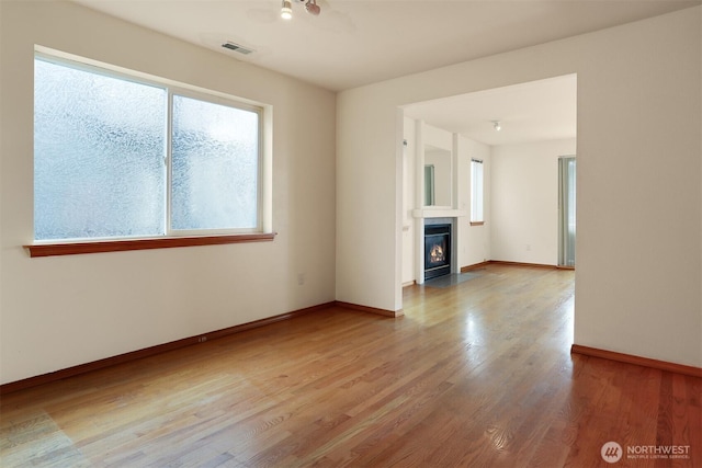 unfurnished room featuring baseboards, a fireplace with flush hearth, visible vents, and wood finished floors