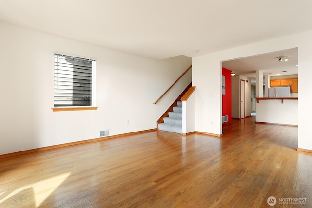 unfurnished living room with visible vents, baseboards, wood finished floors, and stairway