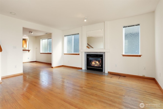 unfurnished living room with baseboards, a fireplace with flush hearth, and wood finished floors