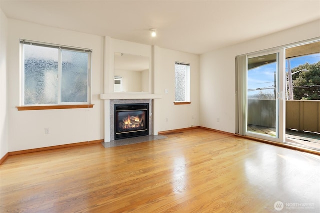 unfurnished living room featuring a fireplace with flush hearth, wood finished floors, and baseboards