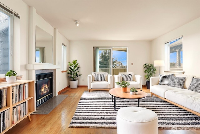 living area featuring light wood-style flooring, a fireplace with flush hearth, and baseboards