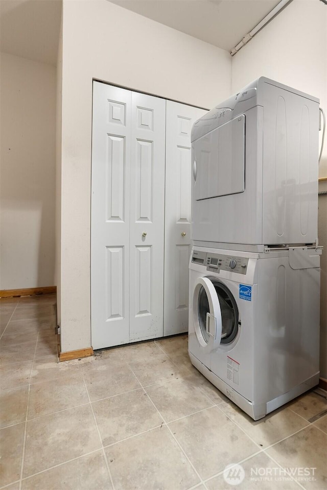 laundry area featuring light tile patterned floors, baseboards, laundry area, and stacked washer / dryer