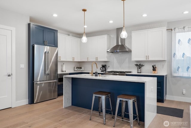 kitchen with high quality fridge, wall chimney exhaust hood, light countertops, and a sink