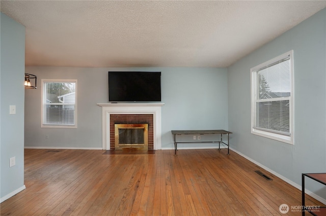 unfurnished living room with hardwood / wood-style flooring, a brick fireplace, baseboards, and visible vents