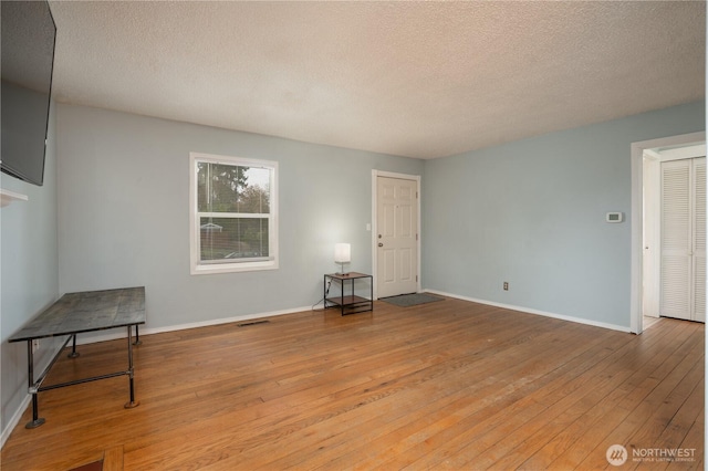 empty room featuring visible vents, baseboards, a textured ceiling, and hardwood / wood-style flooring