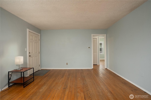 empty room featuring a textured ceiling, baseboards, and hardwood / wood-style flooring