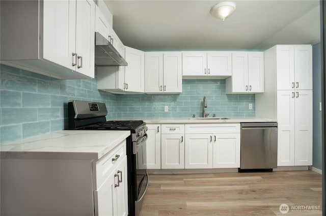 kitchen featuring light stone countertops, under cabinet range hood, light wood-type flooring, stainless steel appliances, and a sink