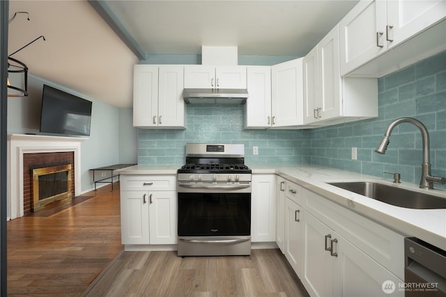 kitchen with a sink, under cabinet range hood, backsplash, wood finished floors, and appliances with stainless steel finishes