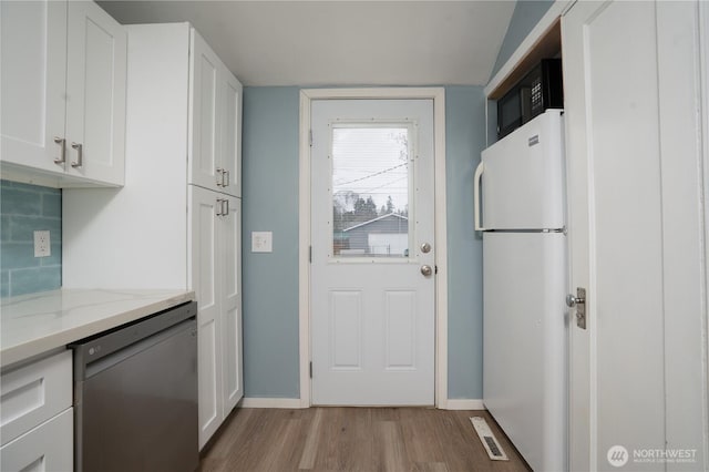 kitchen with light stone counters, light wood finished floors, white cabinetry, freestanding refrigerator, and stainless steel dishwasher