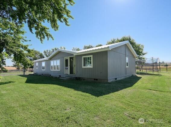 rear view of property featuring a trampoline, a lawn, fence, and crawl space