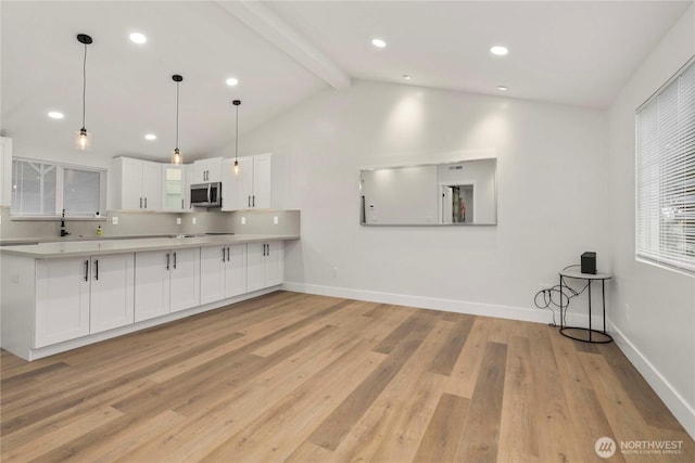 kitchen with light wood finished floors, lofted ceiling with beams, light countertops, white cabinetry, and stainless steel microwave