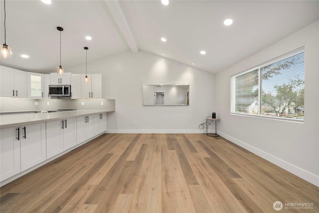 kitchen with stainless steel microwave, vaulted ceiling with beams, baseboards, light wood-type flooring, and white cabinetry