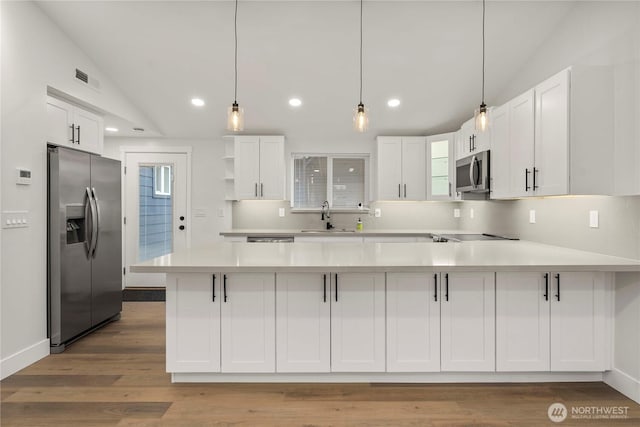 kitchen with lofted ceiling, appliances with stainless steel finishes, a peninsula, white cabinets, and a sink