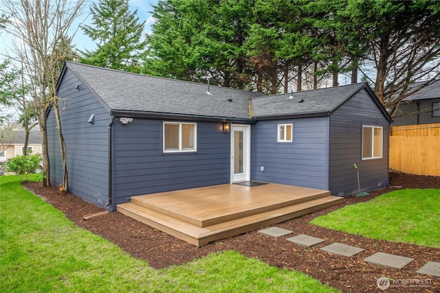 rear view of house with fence, a lawn, roof with shingles, and a wooden deck