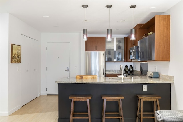 kitchen featuring a peninsula, a sink, stainless steel appliances, glass insert cabinets, and light wood-type flooring