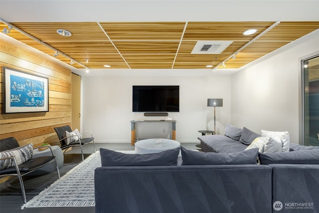 living area featuring track lighting, wooden walls, visible vents, and baseboards