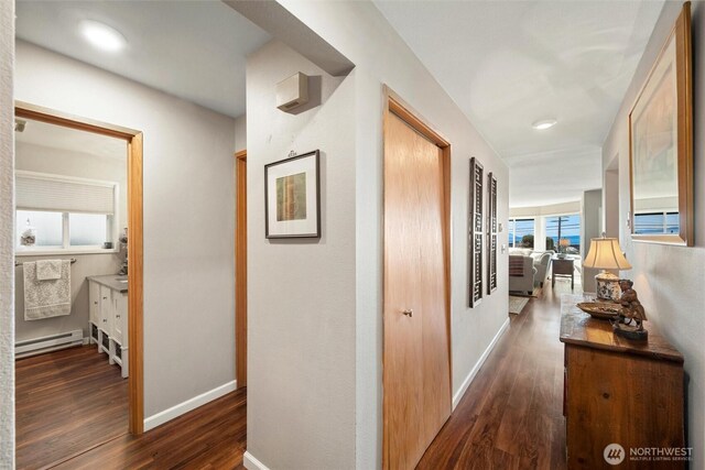 corridor with a baseboard radiator, baseboards, and wood finished floors