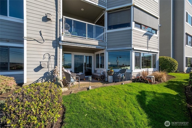 back of property with a balcony, a patio area, and a lawn