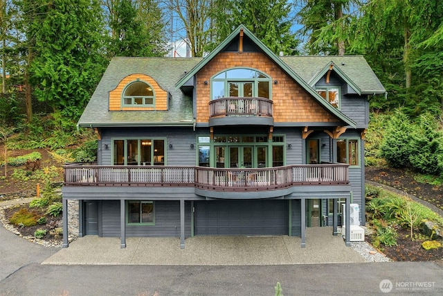 back of property featuring a garage, a balcony, driveway, and a shingled roof